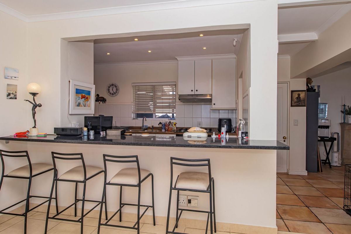 A functional kitchen featuring a granite breakfast bar, built-in cabinetry, and tiled splashbacks, opening into the main living area.