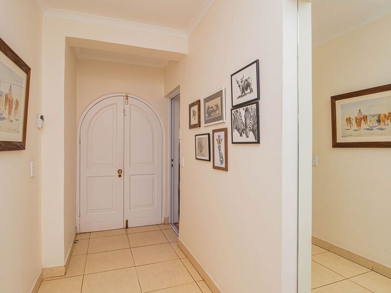 A bright and neutral hallway featuring tiled flooring, coved cornicing, and an elegant arched double door entrance.