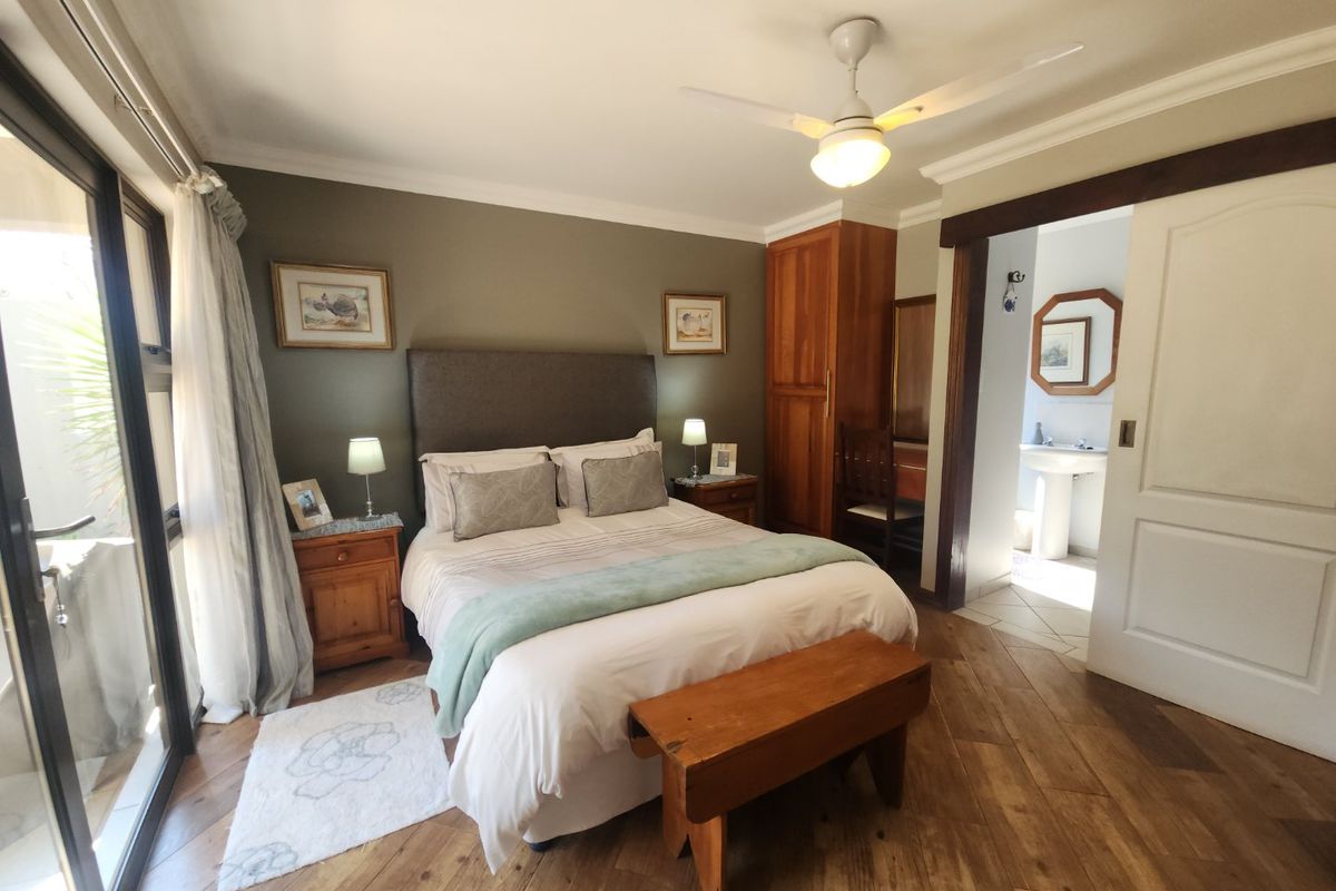 A well-maintained bedroom featuring warm wooden flooring, a ceiling fan, and direct access to an en-suite bathroom through a sliding door.