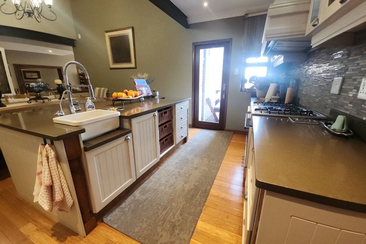 A well-appointed kitchen featuring a farmhouse sink, stone countertops, gas hob, and timber cabinetry, complemented by warm hardwood flooring and a tiled backsplash.