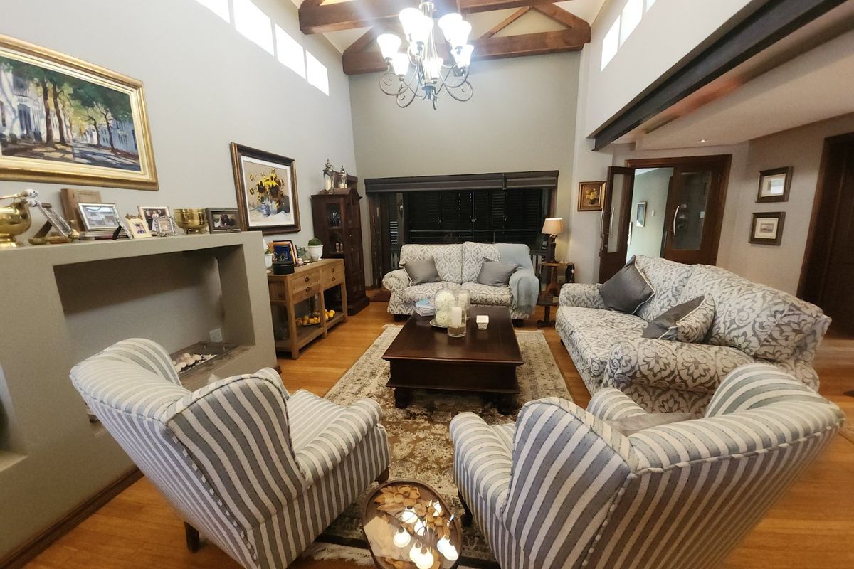 Spacious living room featuring high vaulted ceilings with exposed timber beams, a fireplace, hardwood flooring, and abundant natural light from clerestory windows.