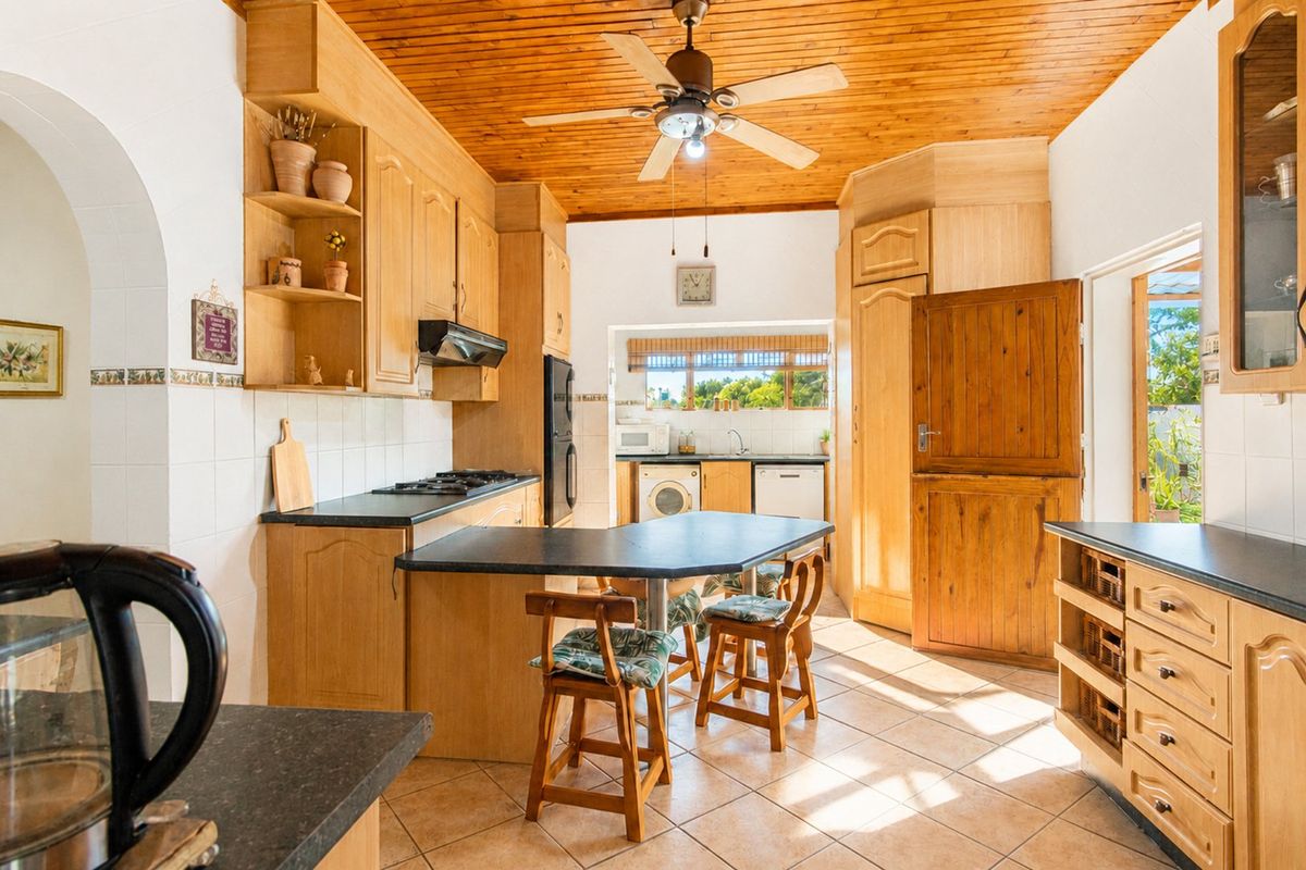 A spacious farmhouse-style kitchen featuring timber ceilings, extensive wooden cabinetry, a breakfast bar, and a functional scullery area with direct outdoor access.