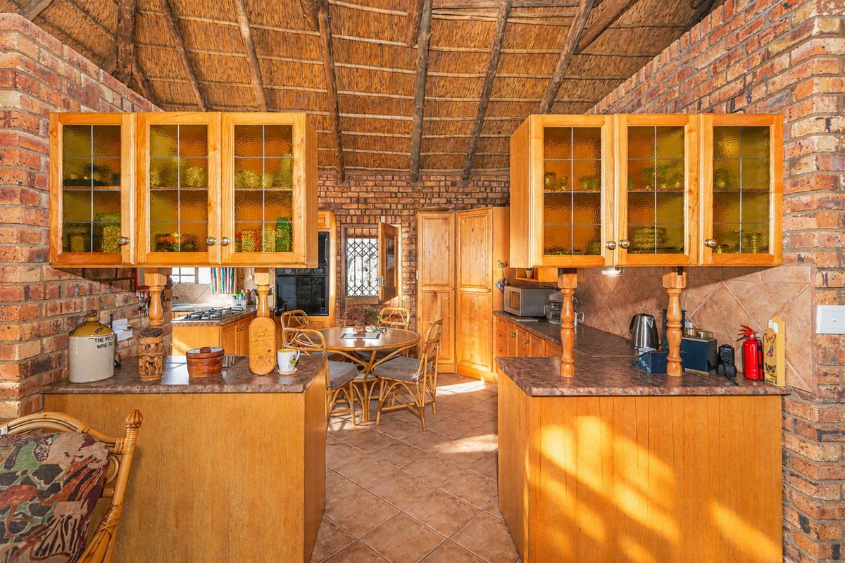 Rustic kitchen featuring exposed brick walls, a high thatched ceiling, timber cabinetry, and tiled flooring, offering a warm and traditional farm-style aesthetic.