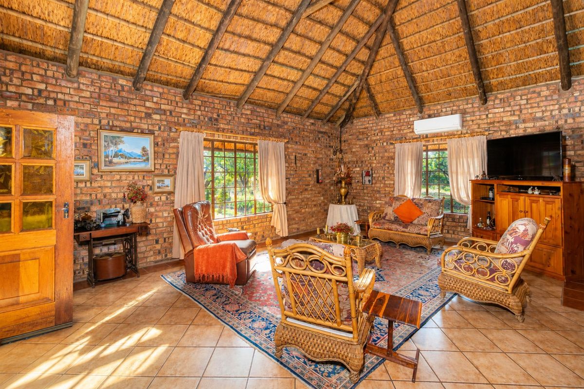 Spacious living room featuring rustic exposed brick walls, a high vaulted thatched ceiling with timber rafters, and ceramic tiled flooring.