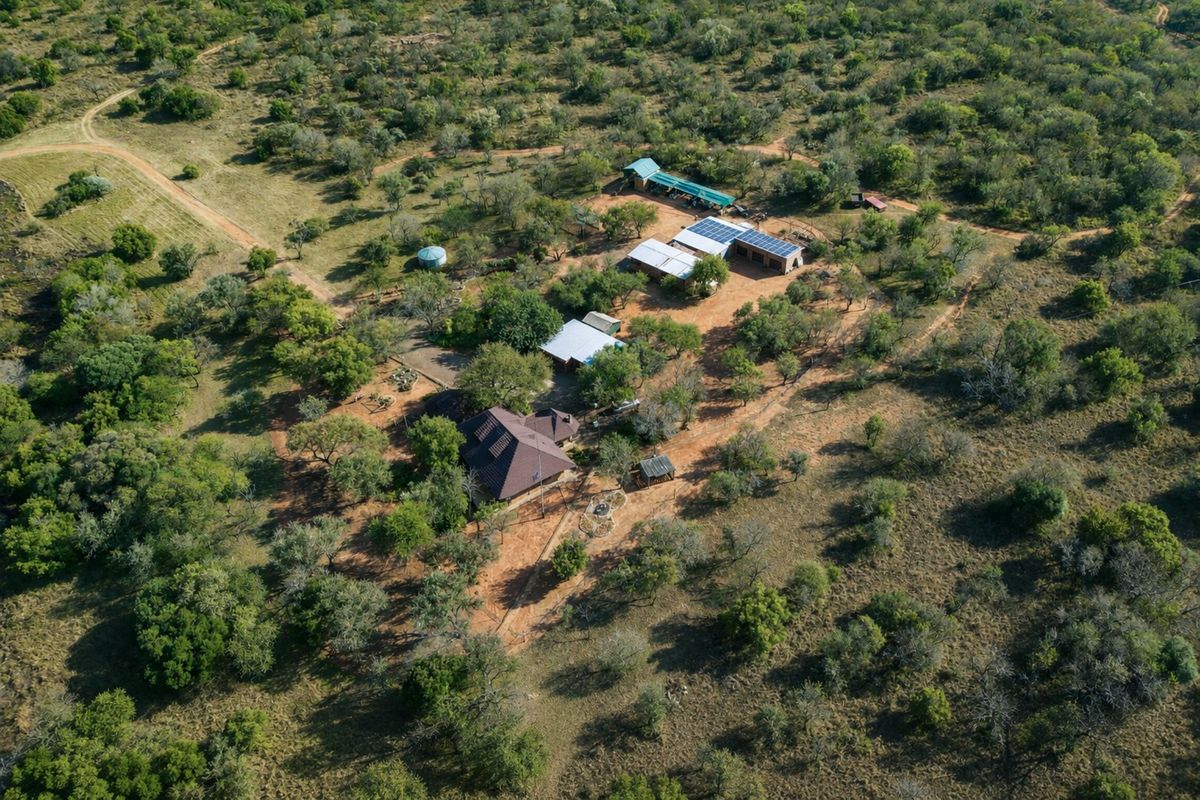 Aerial view of a rural farm property featuring multiple outbuildings, solar panel installations, and surrounding natural bushveld landscape.