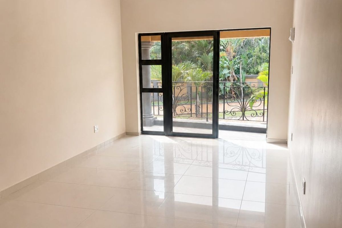 A bright, empty living room featuring polished porcelain floor tiles, recessed ceiling lighting, and a sliding glass door leading to a private balcony.