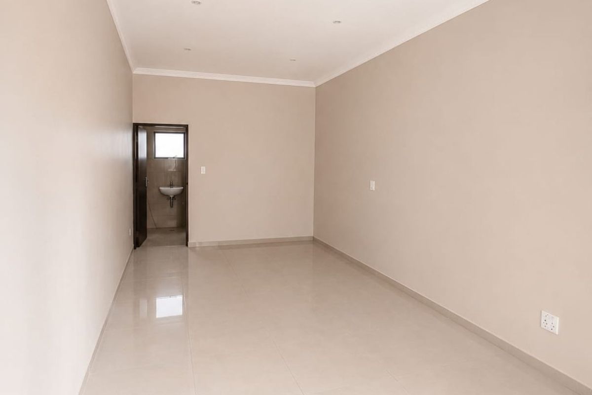 A spacious, empty commercial room featuring neutral wall finishes, tiled flooring, recessed ceiling lighting, and an adjoining small washroom area.