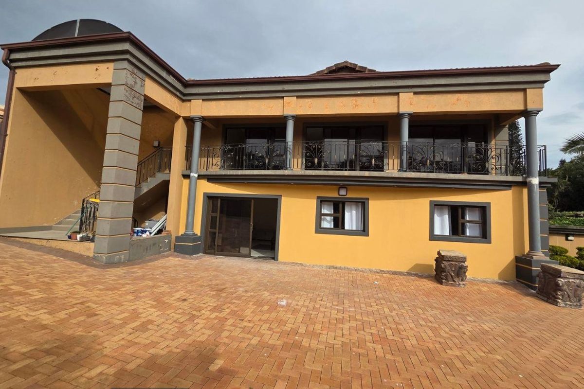 Exterior view of a commercial property featuring a paved courtyard, covered balcony with decorative railings, and multi-level architectural design.