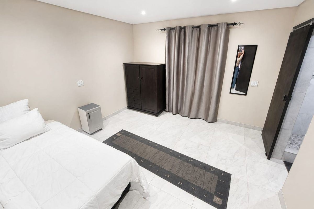 A spacious bedroom featuring neutral wall tones, tiled flooring, recessed lighting, and an en-suite bathroom access point.