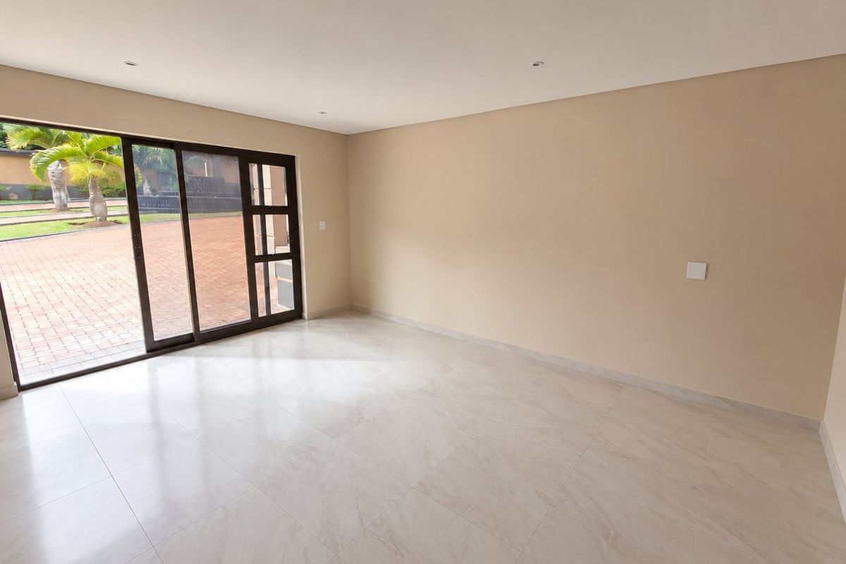 A bright, empty living room featuring neutral tiled flooring, recessed lighting, and large sliding glass doors providing direct access to the outdoor patio area.