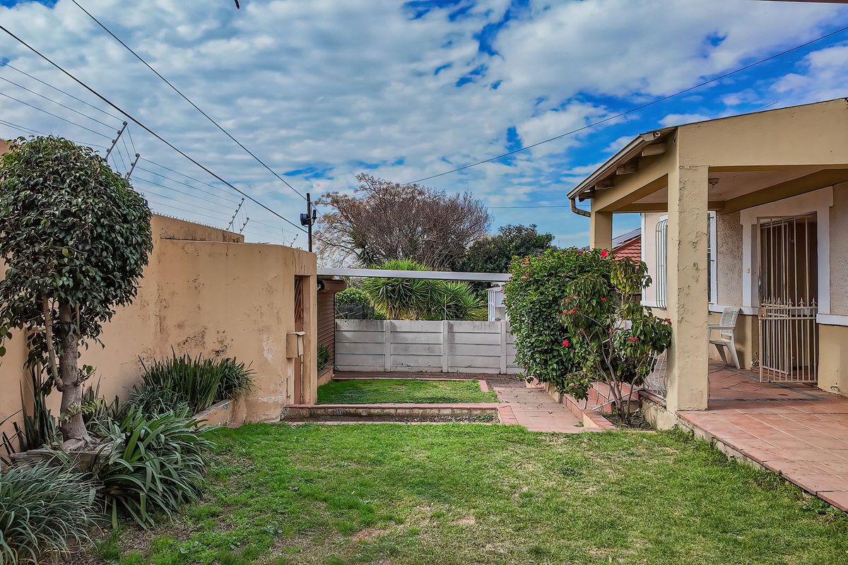 A rear garden view featuring a covered tiled patio, security gate, and established lawn area enclosed by perimeter walls with electric fencing.