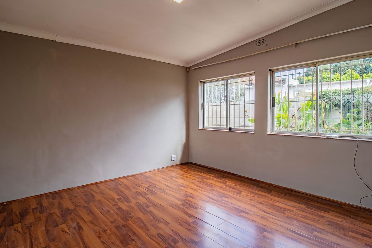 A vacant bedroom featuring laminate flooring, neutral wall tones, and security bars on the windows, offering a blank canvas for personalization.