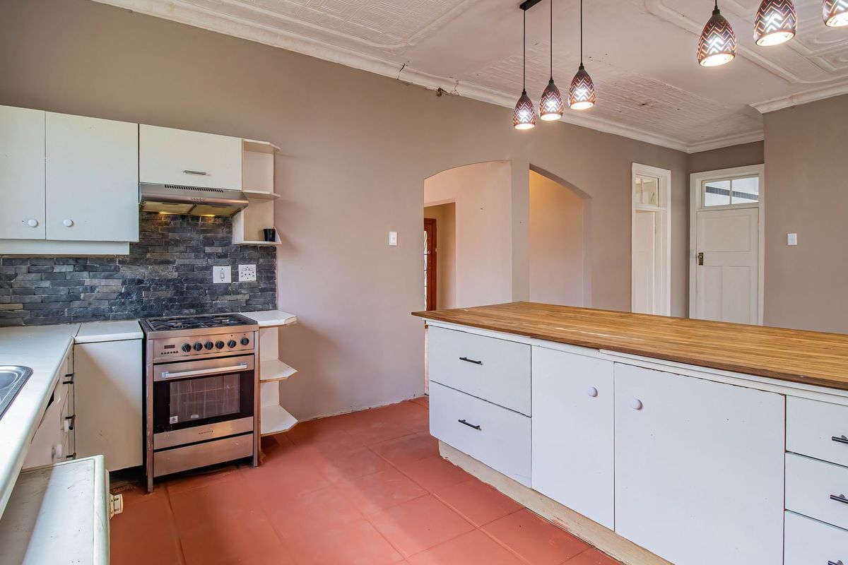A kitchen featuring a freestanding gas stove, stone backsplash, kitchen island with wooden countertop, and decorative pressed metal ceilings.