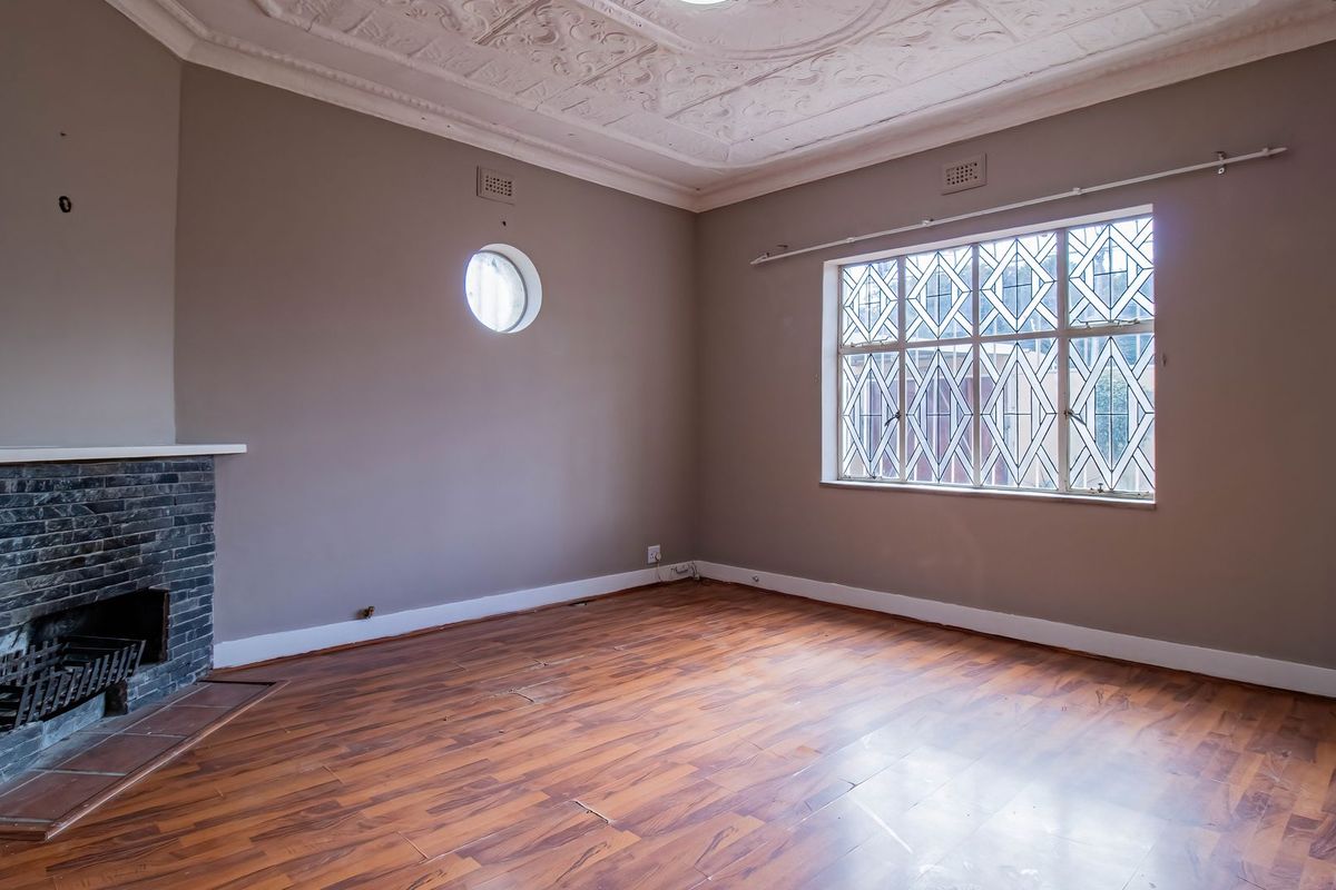 Spacious living room featuring an ornate plaster ceiling, a stone fireplace, and unique leaded glass windows with timber flooring.