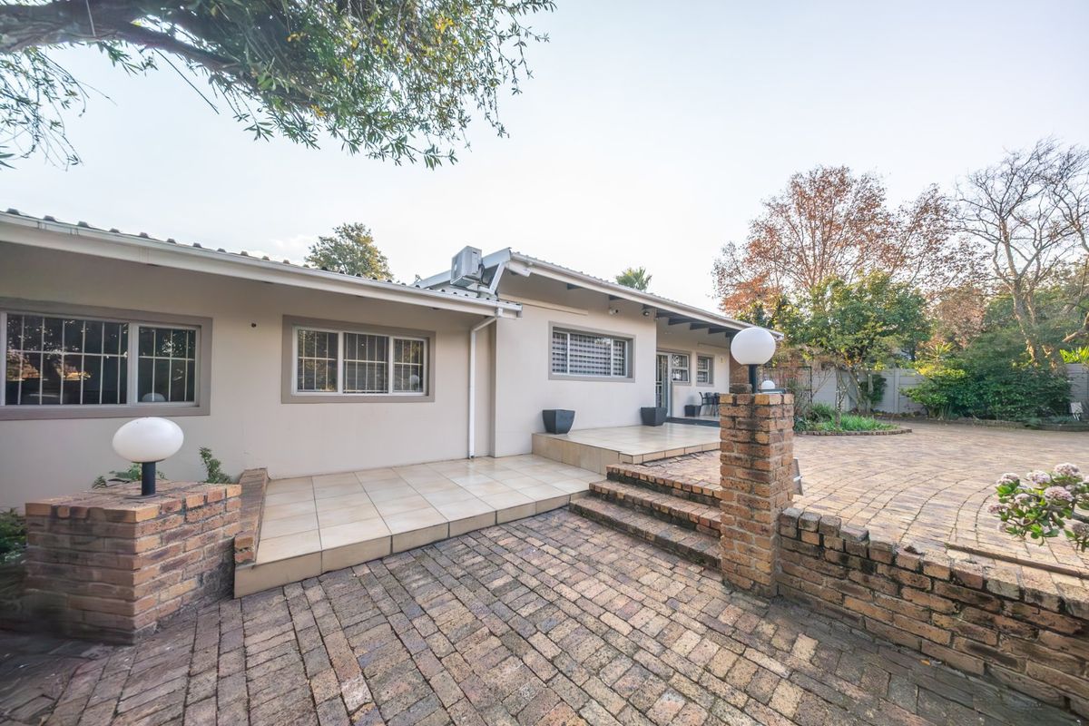 Rear exterior view featuring a paved patio area, brick retaining walls, and tiled terrace leading to the main house structure.