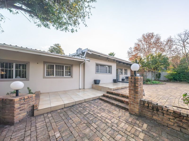 Rear exterior view featuring a paved patio area, brick retaining walls, and tiled terrace leading to the main house structure.