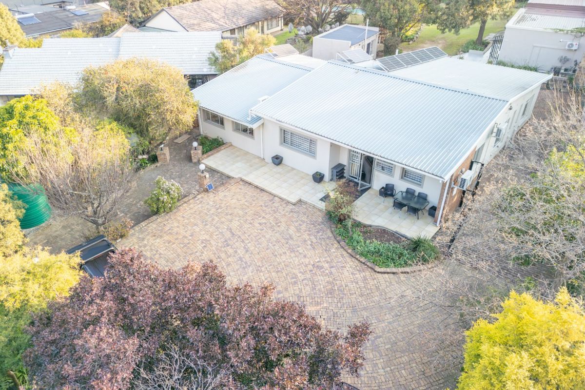 Aerial view of a residential property featuring a large paved driveway, tiled patio area, and a corrugated metal roof with installed solar panels.