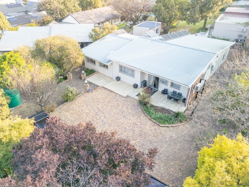 Aerial view of a residential property featuring a large paved driveway, tiled patio area, and a corrugated metal roof with installed solar panels.