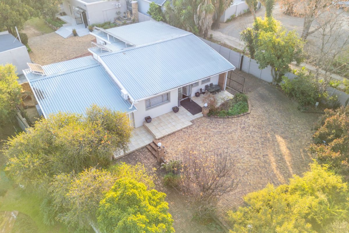 Aerial view of a residential property featuring a corrugated metal roof, paved driveway, and a tiled patio area.