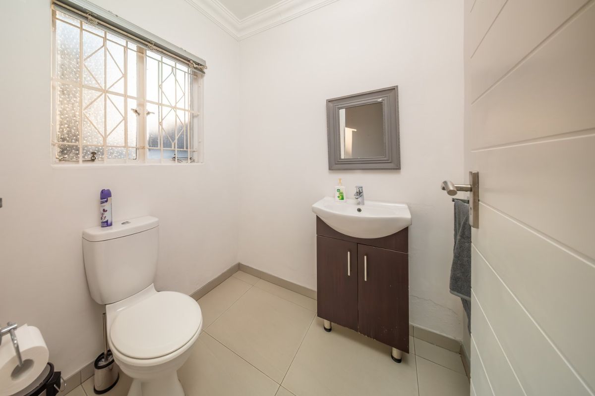 A functional guest bathroom featuring a toilet, vanity basin, tiled flooring, and security bars on the window.