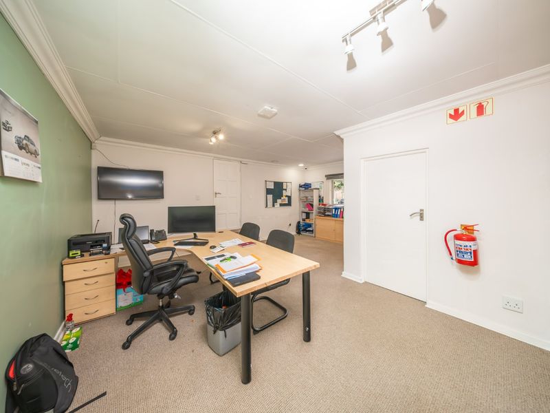 A functional office space featuring neutral carpeting, track lighting, and a dedicated workspace area with built-in fire safety equipment.