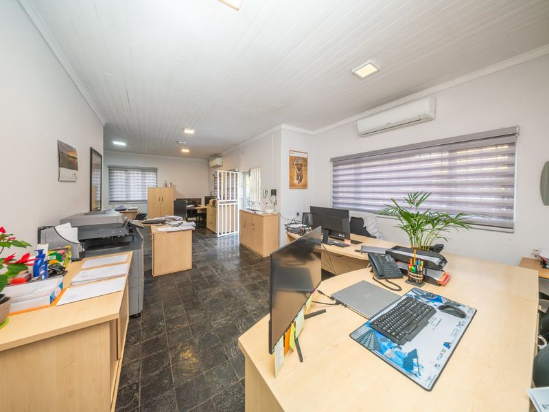A functional office space featuring tiled flooring, a slatted ceiling, and a wall-mounted split-system air conditioning unit.