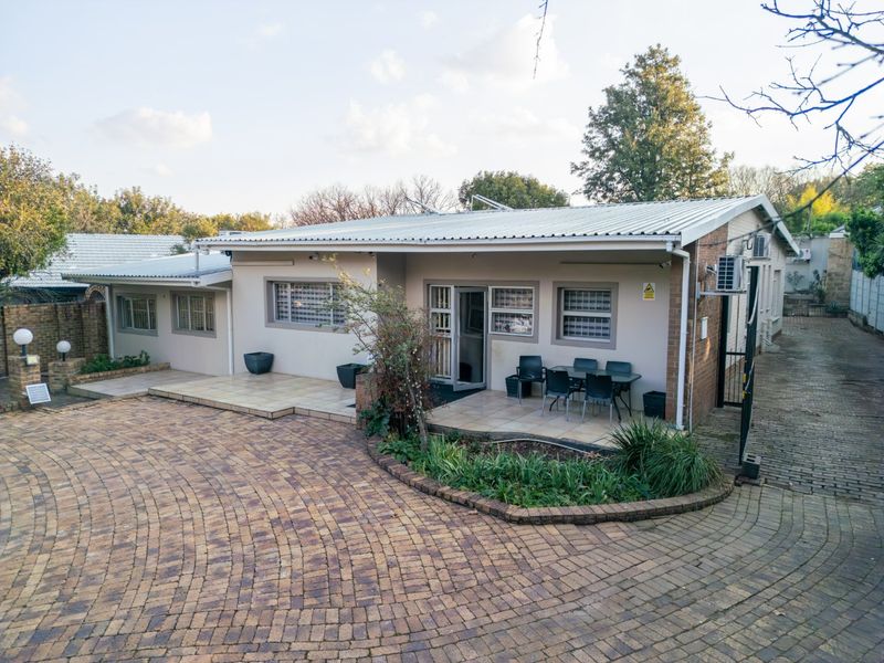 Front view of a single-story residence featuring a brick paved driveway, tiled patio areas, and secure window bars.