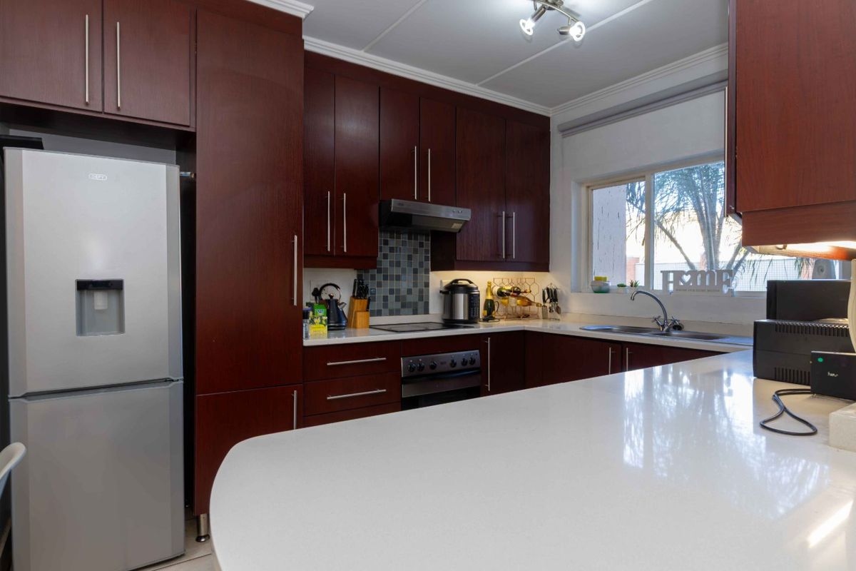 Modern kitchen featuring dark wood cabinetry, stone countertops, built-in oven, electric hob, and a functional layout with ample storage and workspace.