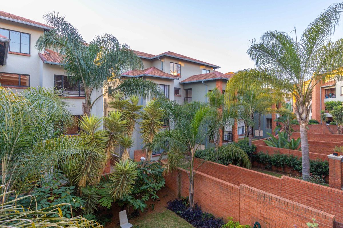 A view of the rear townhouse facade featuring established garden landscaping, brick boundary walls, and a multi-story architectural design with tiled roofing.