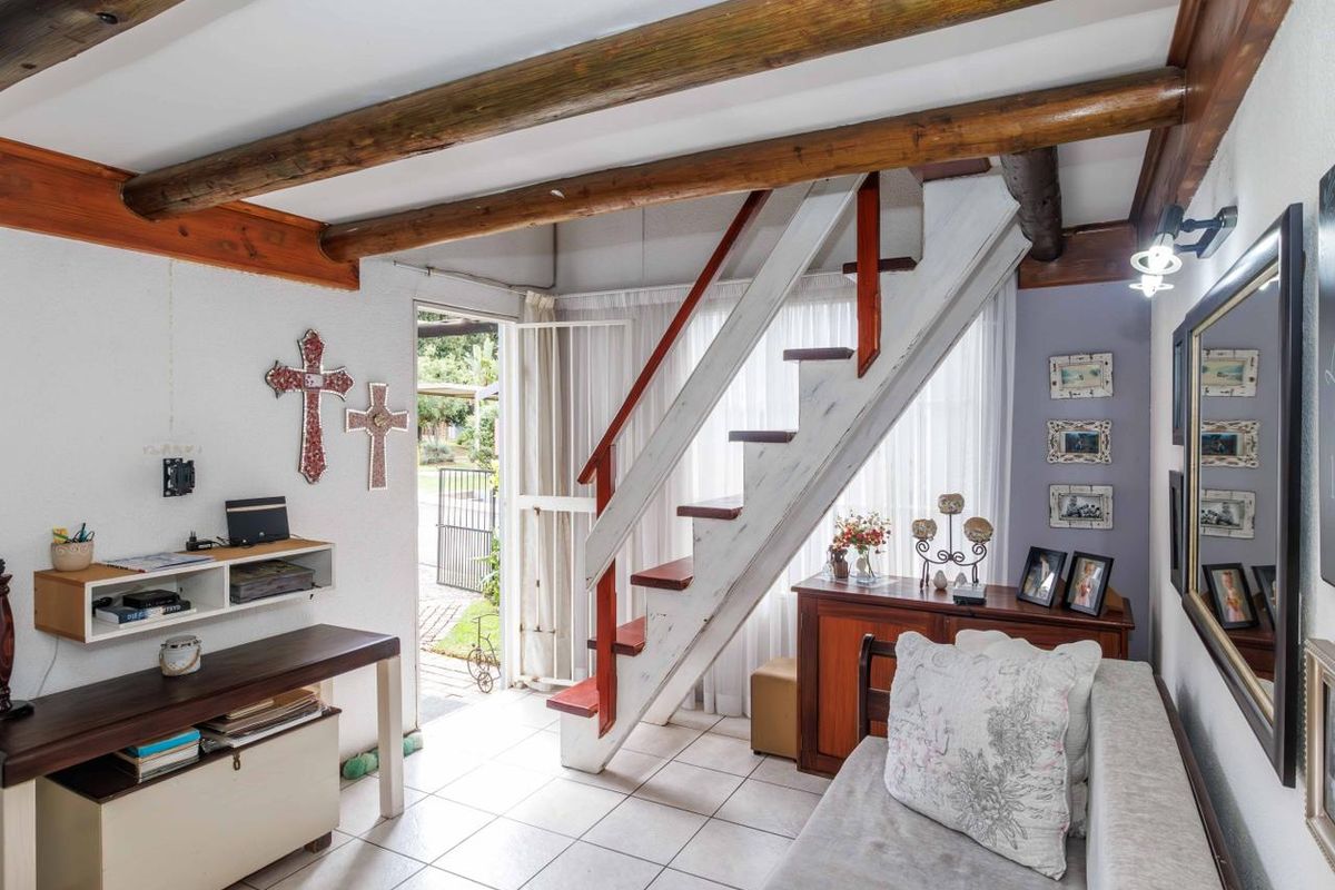 Living area featuring exposed timber ceiling beams, tiled flooring, and a staircase leading to the upper level with direct access to the exterior.