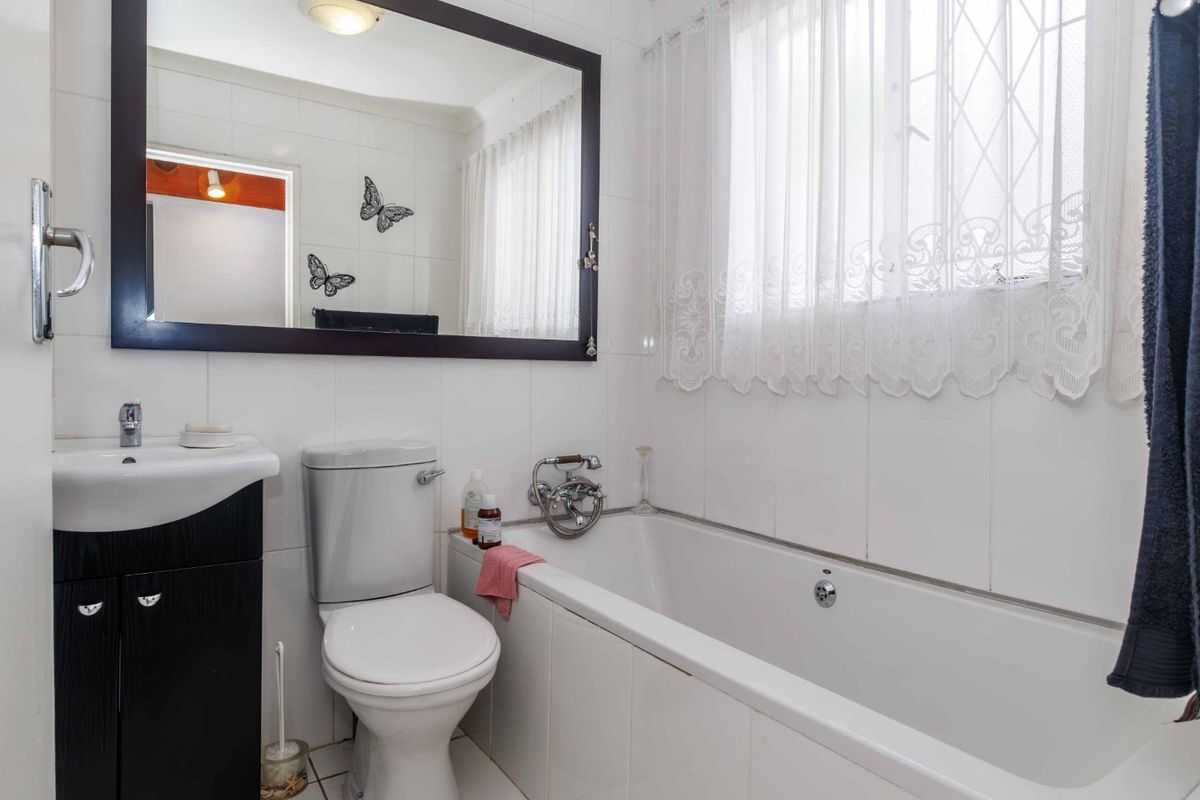 A functional bathroom featuring a vanity cabinet, basin, toilet, and bathtub with tiled finishes and a large wall-mounted mirror.