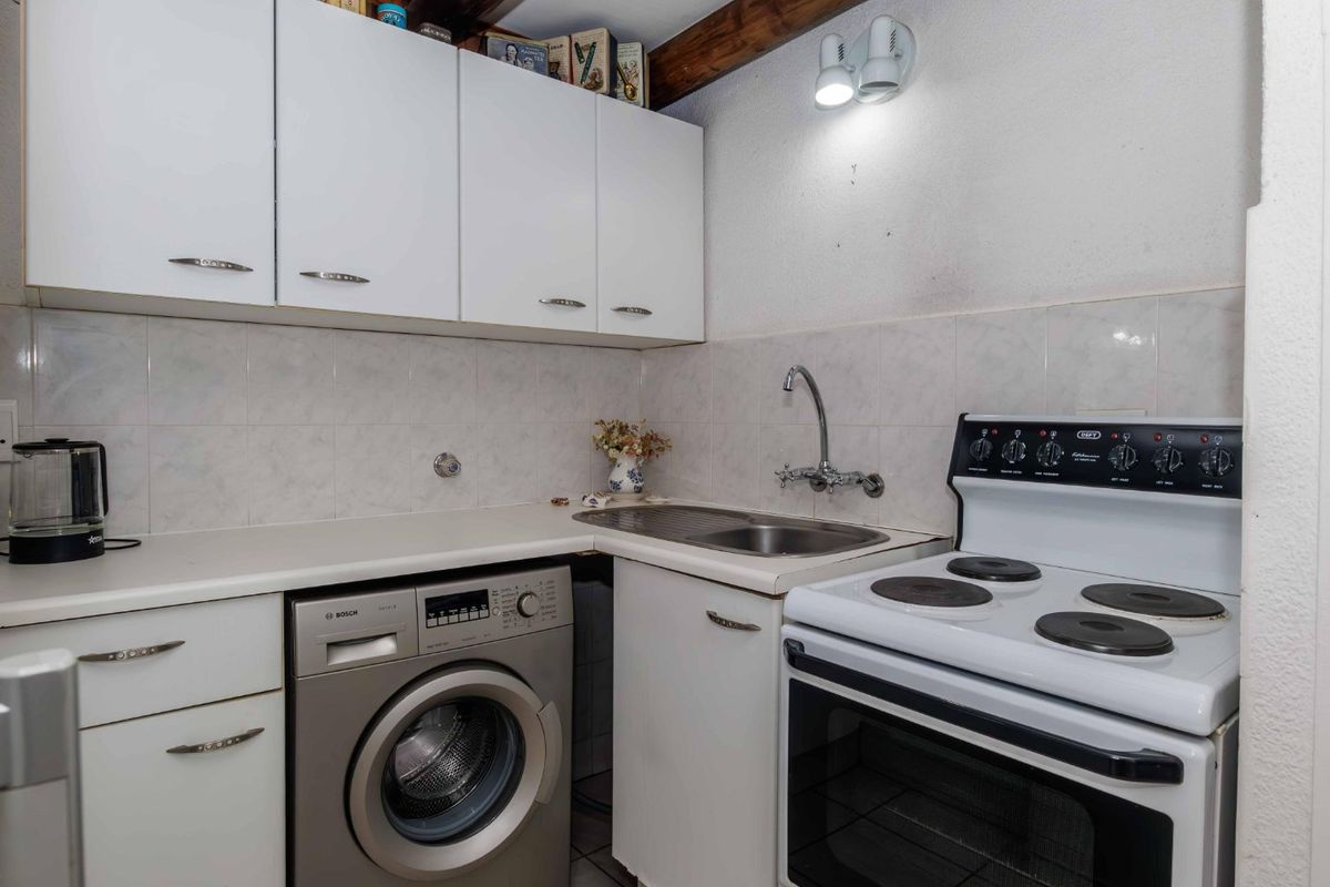 Compact kitchen featuring white cabinetry, tiled backsplash, exposed timber ceiling beams, and integrated laundry facilities with a freestanding electric stove.