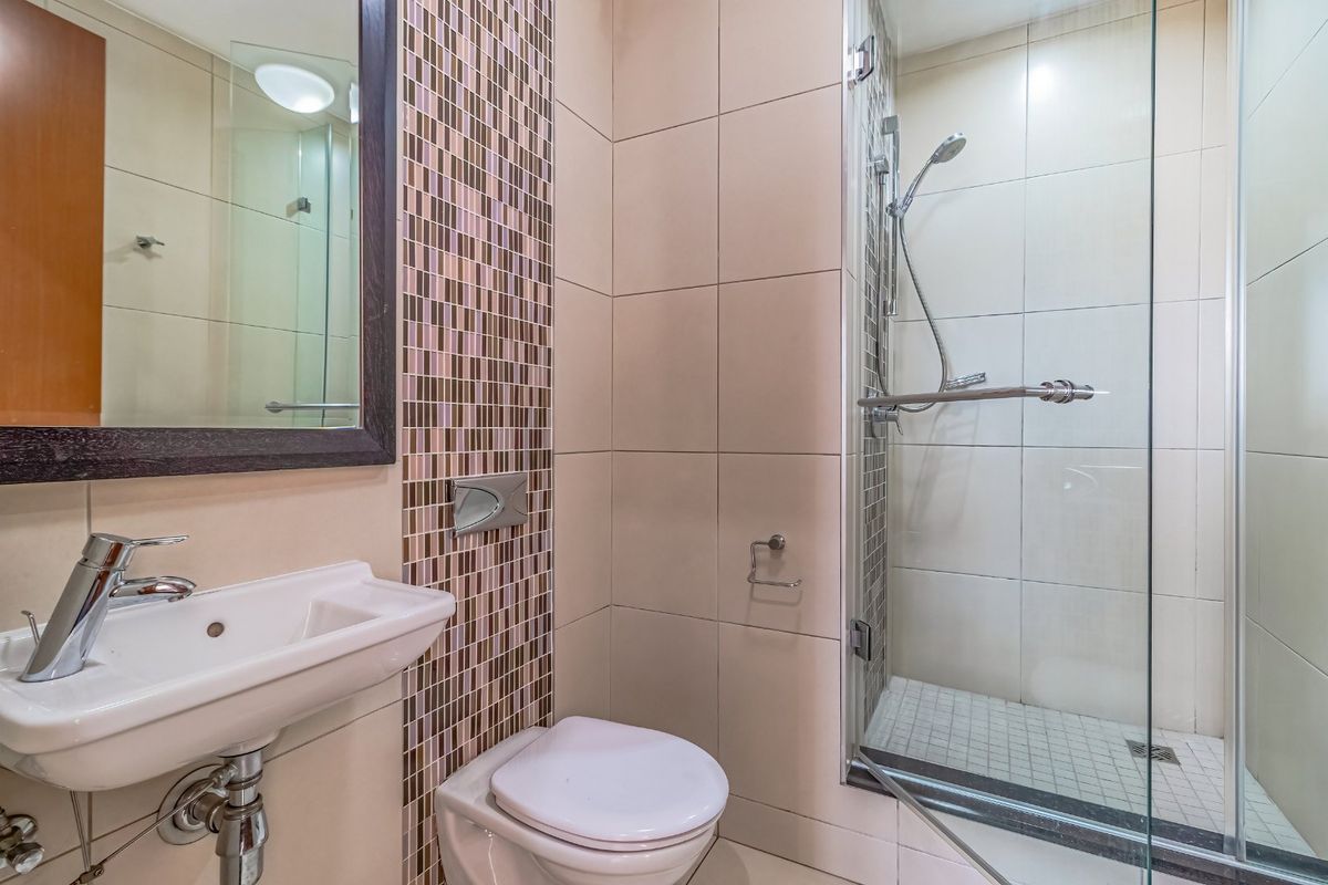 A compact, modern bathroom featuring a wall-hung toilet, wall-mounted basin, and a glass-enclosed shower with mosaic tile accents.