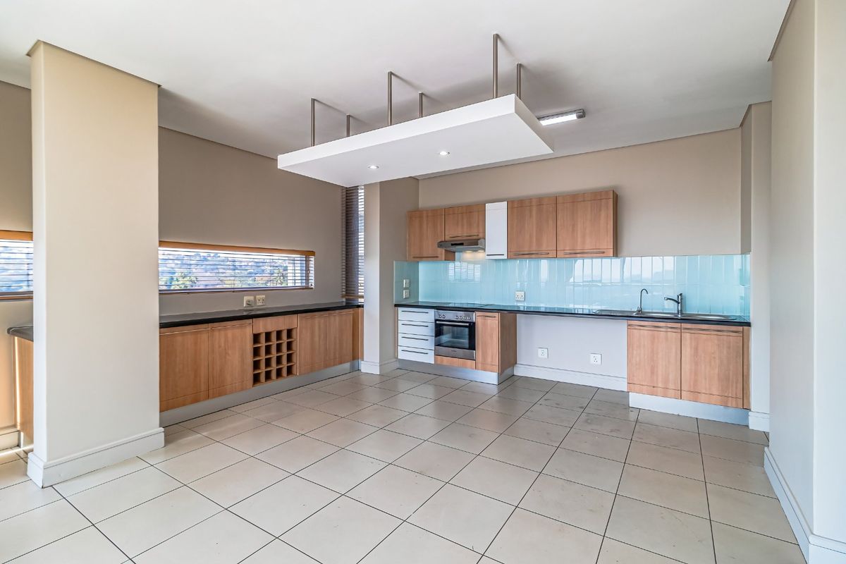 A spacious, empty kitchen featuring wood-finish cabinetry, integrated appliances, a tiled splashback, and a unique suspended ceiling feature with recessed lighting.
