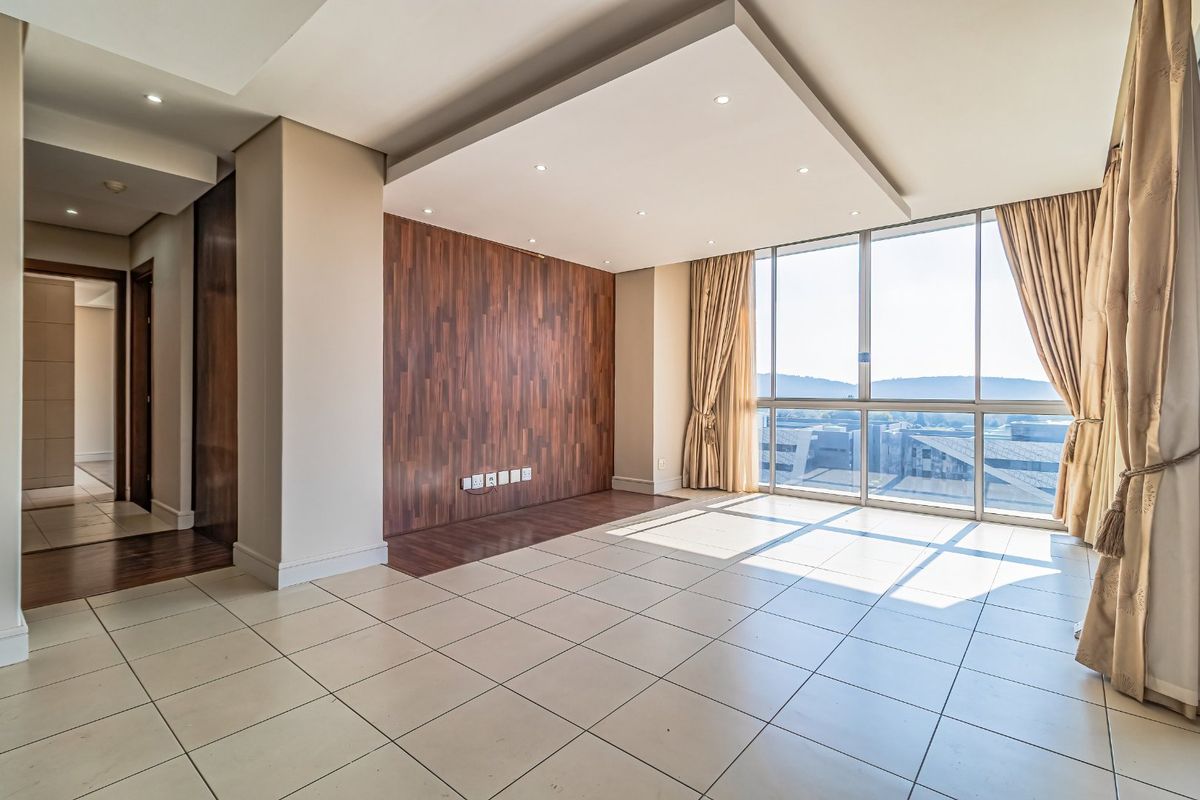 Spacious living area featuring large floor-to-ceiling windows, a modern wood veneer feature wall, recessed ceiling lighting, and neutral tiled flooring.