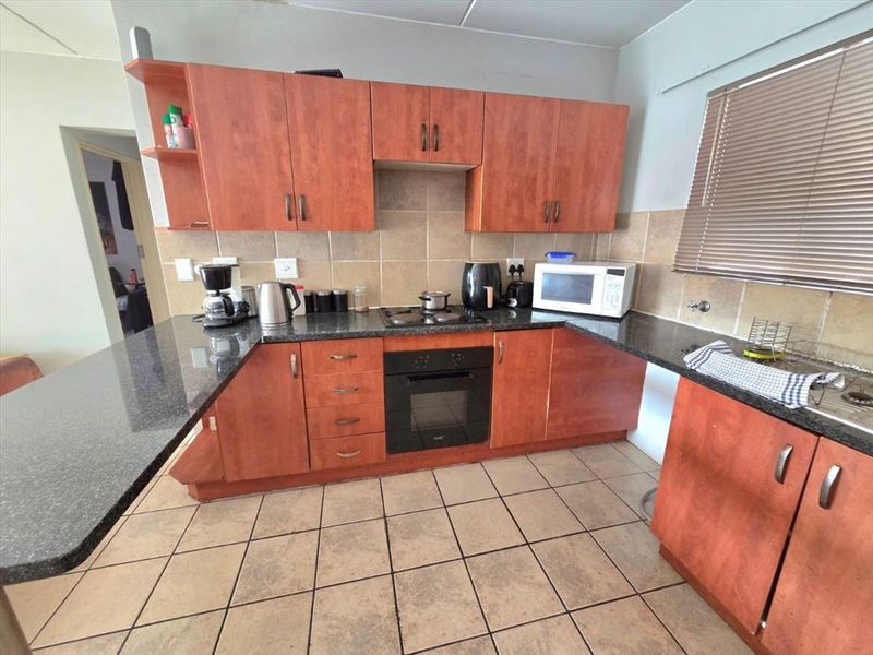 A functional kitchen featuring granite countertops, built-in oven, hob, and ample laminate cabinetry with tiled backsplash and flooring.