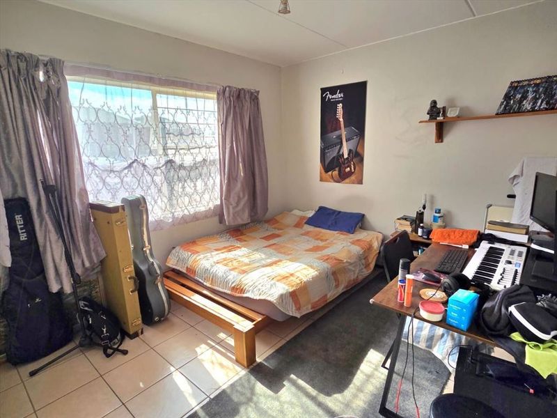 A bedroom featuring tiled flooring and a large window, providing natural light. The space requires cosmetic updates to improve its overall condition.