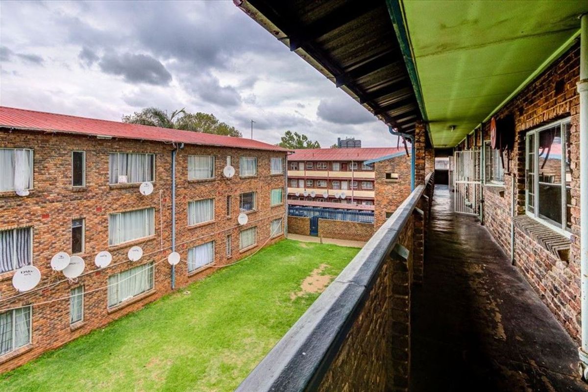 An exterior view from a communal apartment balcony overlooking a central courtyard and surrounding brick residential buildings.