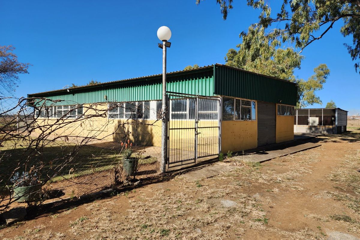 Rear view of a farm outbuilding featuring a corrugated metal roof, security gate, and concrete walkway on a rural property.