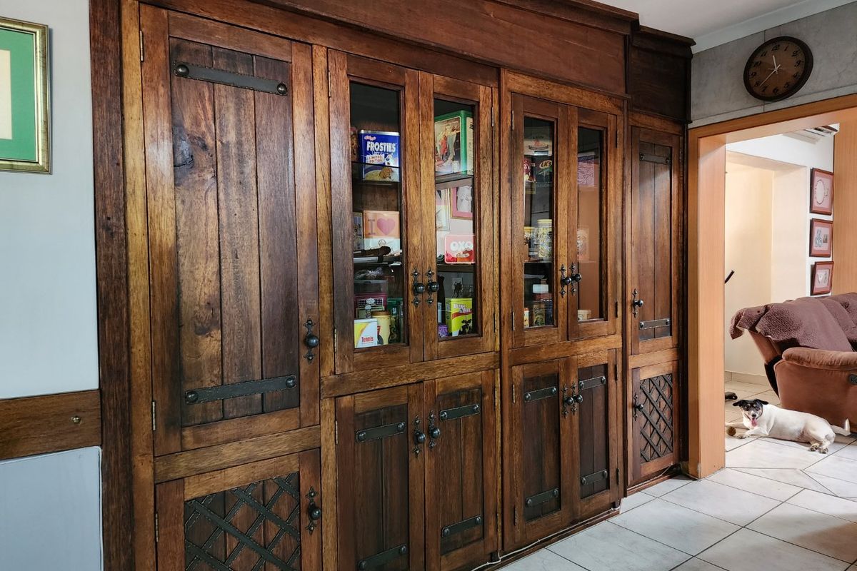 A living area featuring extensive custom-built wooden cabinetry with glass display sections and decorative lattice detailing, complemented by neutral tiled flooring.