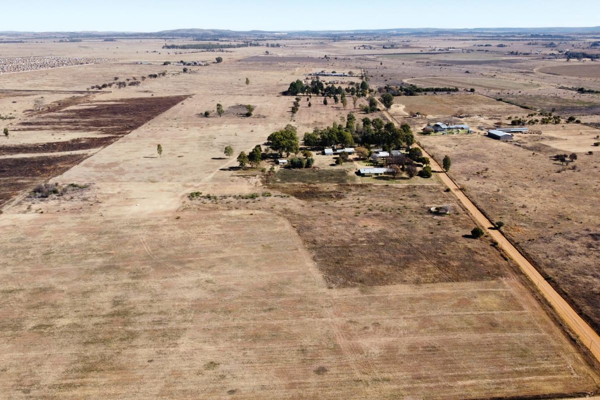An aerial view of a large rural farm property featuring expansive open fields, a dirt access road, and a cluster of farm buildings.