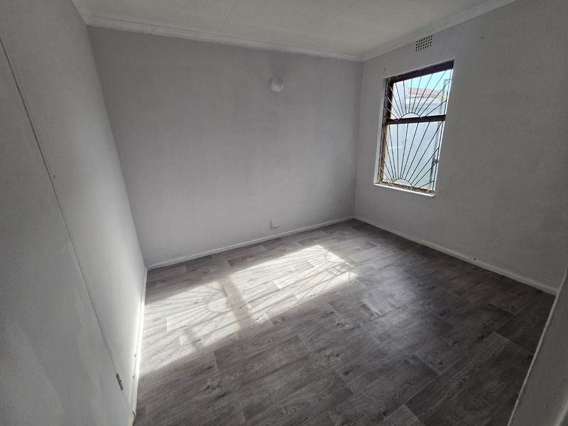 An empty bedroom featuring grey laminate flooring, neutral walls, and a window fitted with a decorative security gate.
