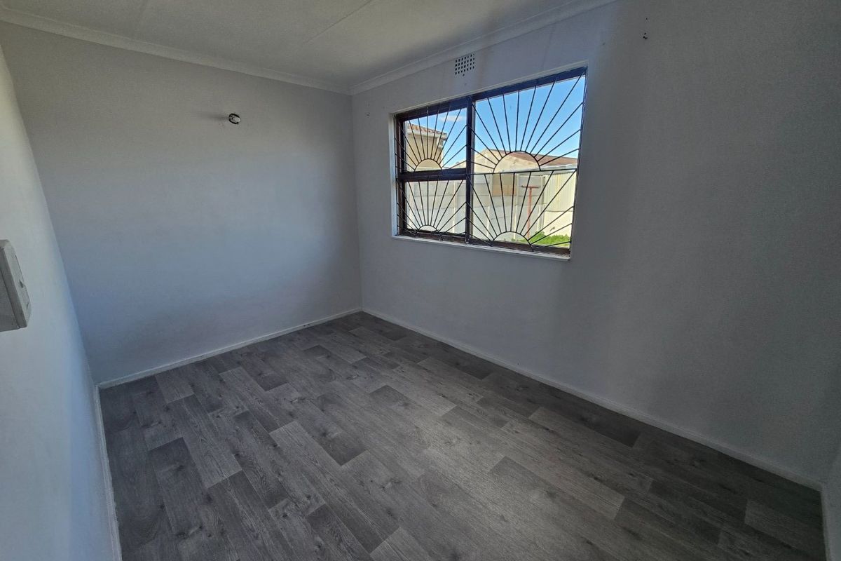 An empty bedroom featuring grey laminate flooring, white walls, and a window fitted with security bars.