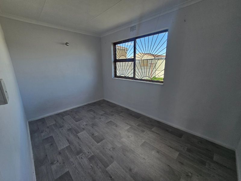 An empty bedroom featuring grey laminate flooring, white walls, and a window fitted with security bars.