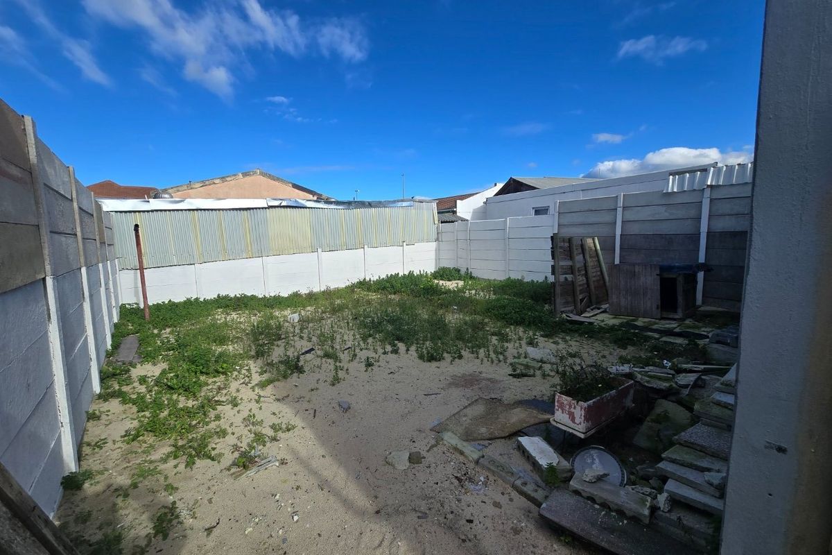 A rear outdoor space featuring a precast concrete boundary wall and corrugated metal fencing, currently requiring significant landscaping and ground surface improvements.