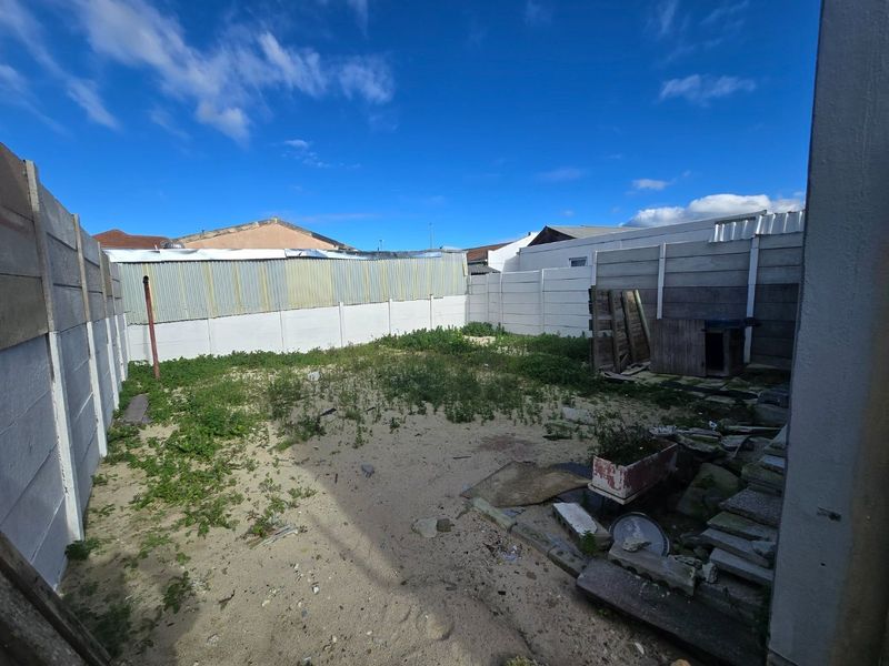 A rear outdoor space featuring a precast concrete boundary wall and corrugated metal fencing, currently requiring significant landscaping and ground surface improvements.