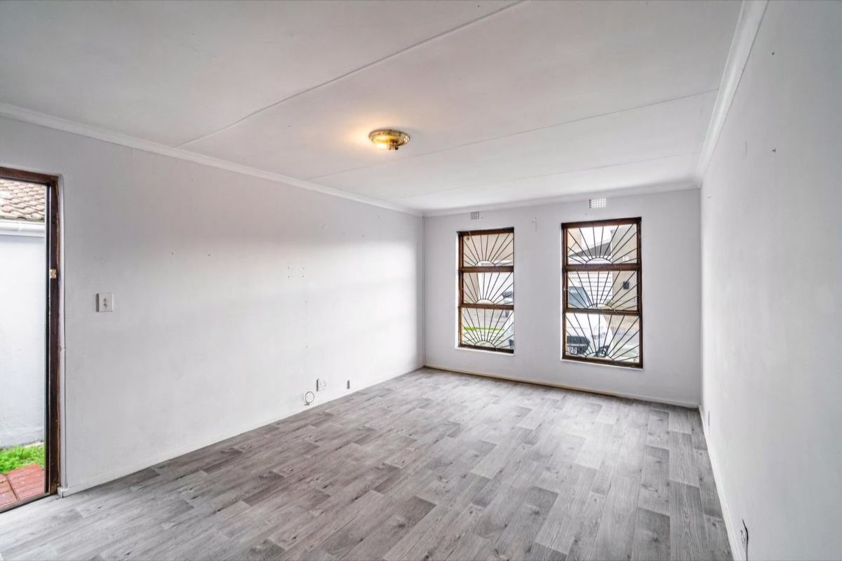 An empty living room featuring modern grey laminate flooring, white walls, and windows fitted with decorative security bars.