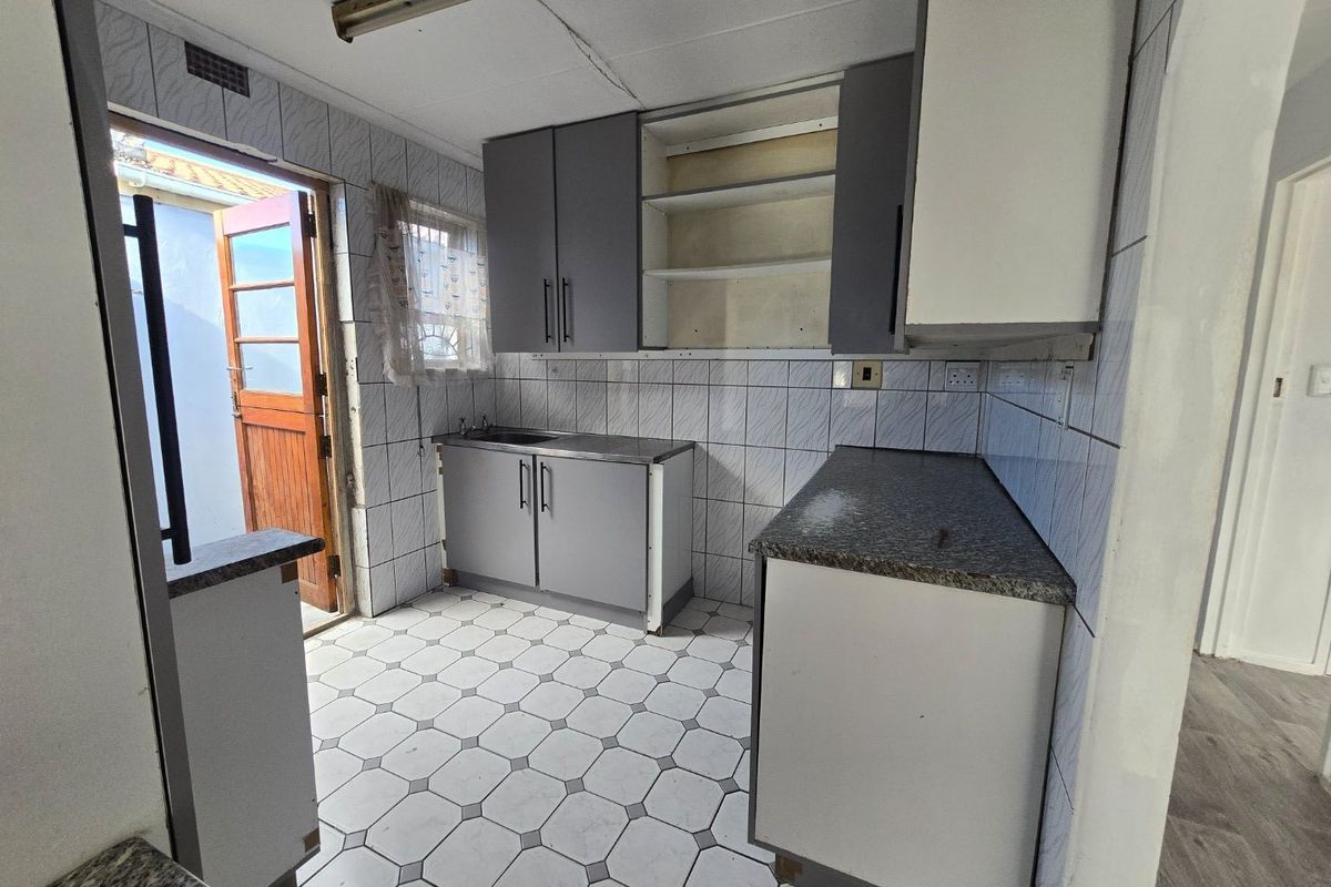 A functional kitchen space featuring tiled finishes, built-in cabinetry, and direct access to an outdoor area, offering potential for modernization and cosmetic updates.