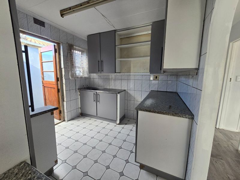 A functional kitchen space featuring tiled finishes, built-in cabinetry, and direct access to an outdoor area, offering potential for modernization and cosmetic updates.