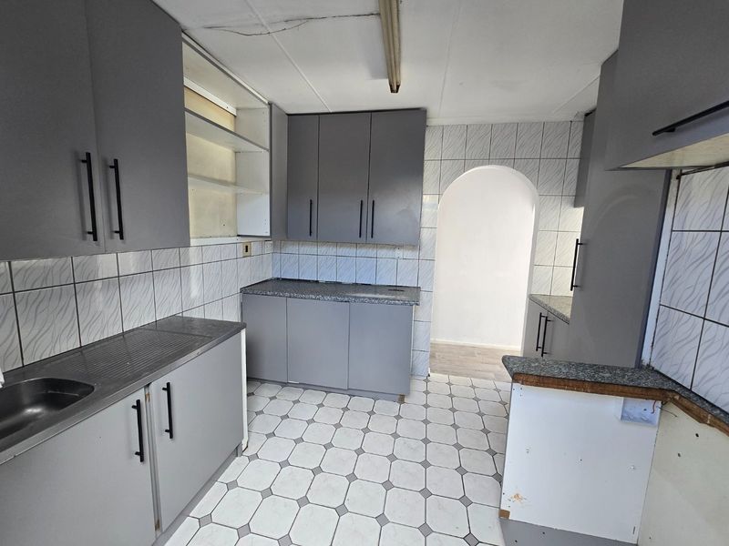 A functional kitchen space featuring grey cabinetry, tiled splashbacks, and tiled flooring, currently vacant and ready for renovation or modernization.